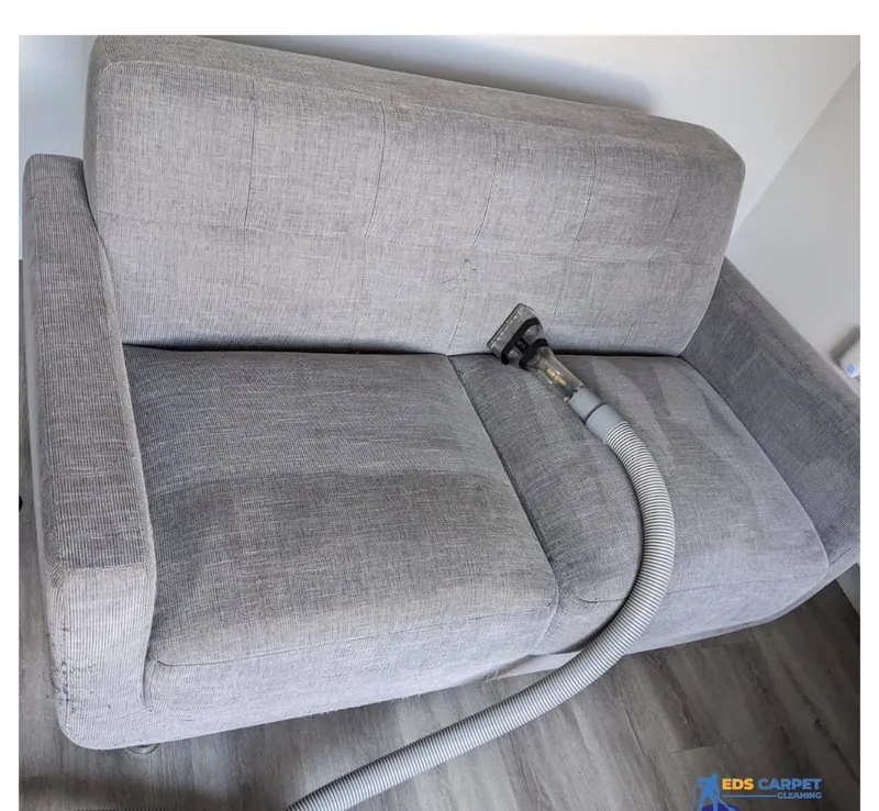 Grey fabric sofa being cleaned with an upholstery tool